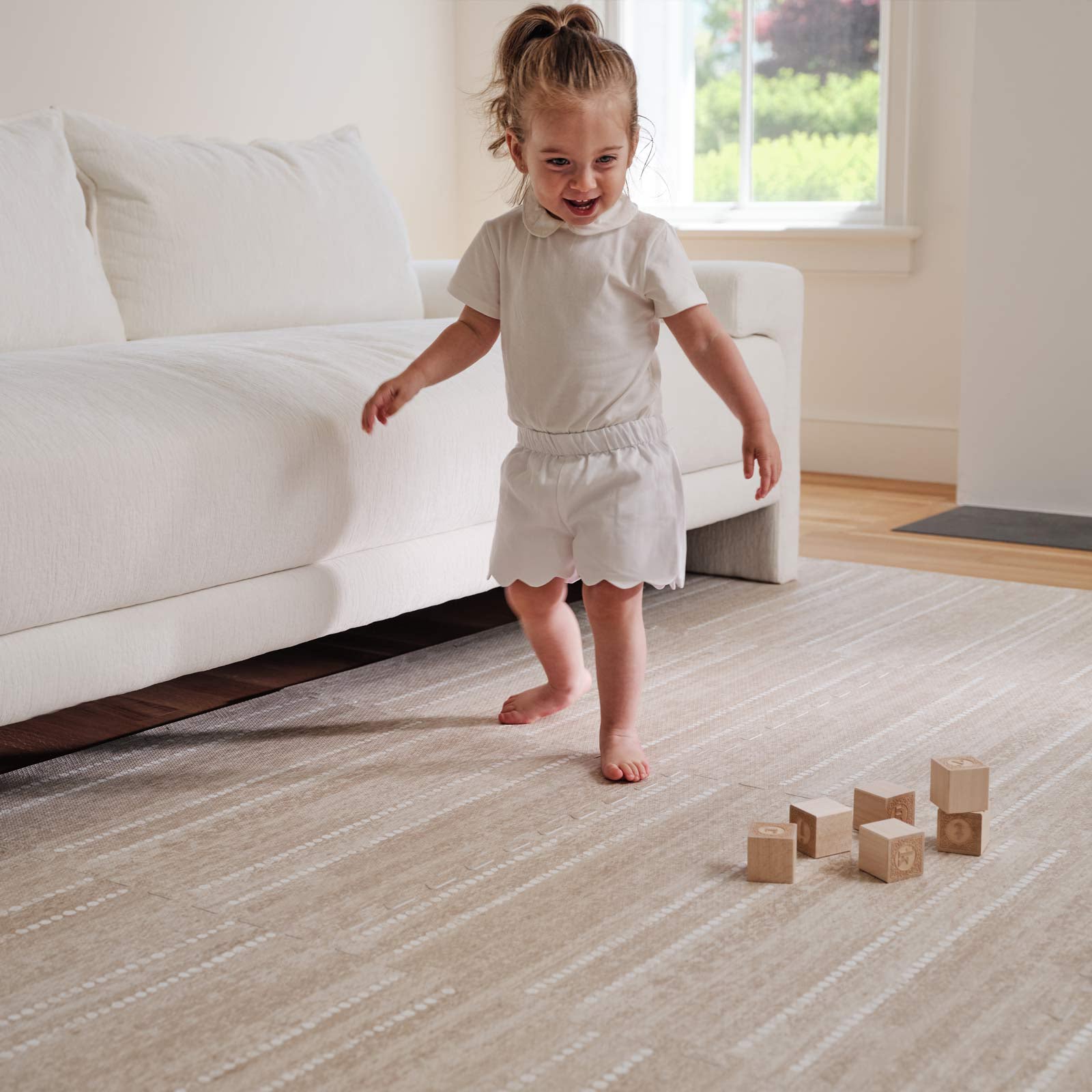 Aspen toast neutral minimal stripe little nomad play mat shown in a living room with toddler running and wooden blocks on the mat