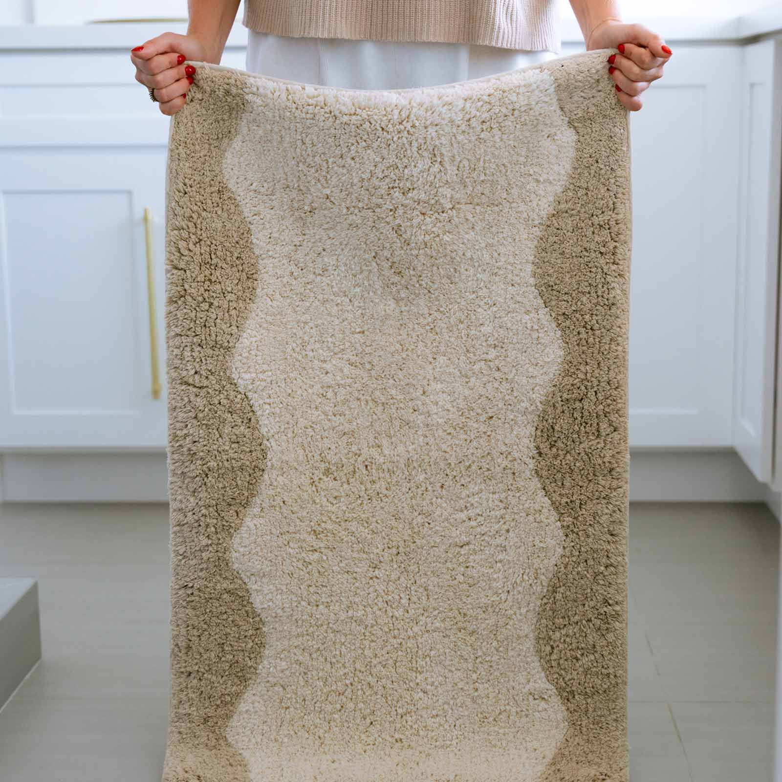 Harper au lait beige scallop print bath mat in size 21x58 with woman holding up the mat by the corners