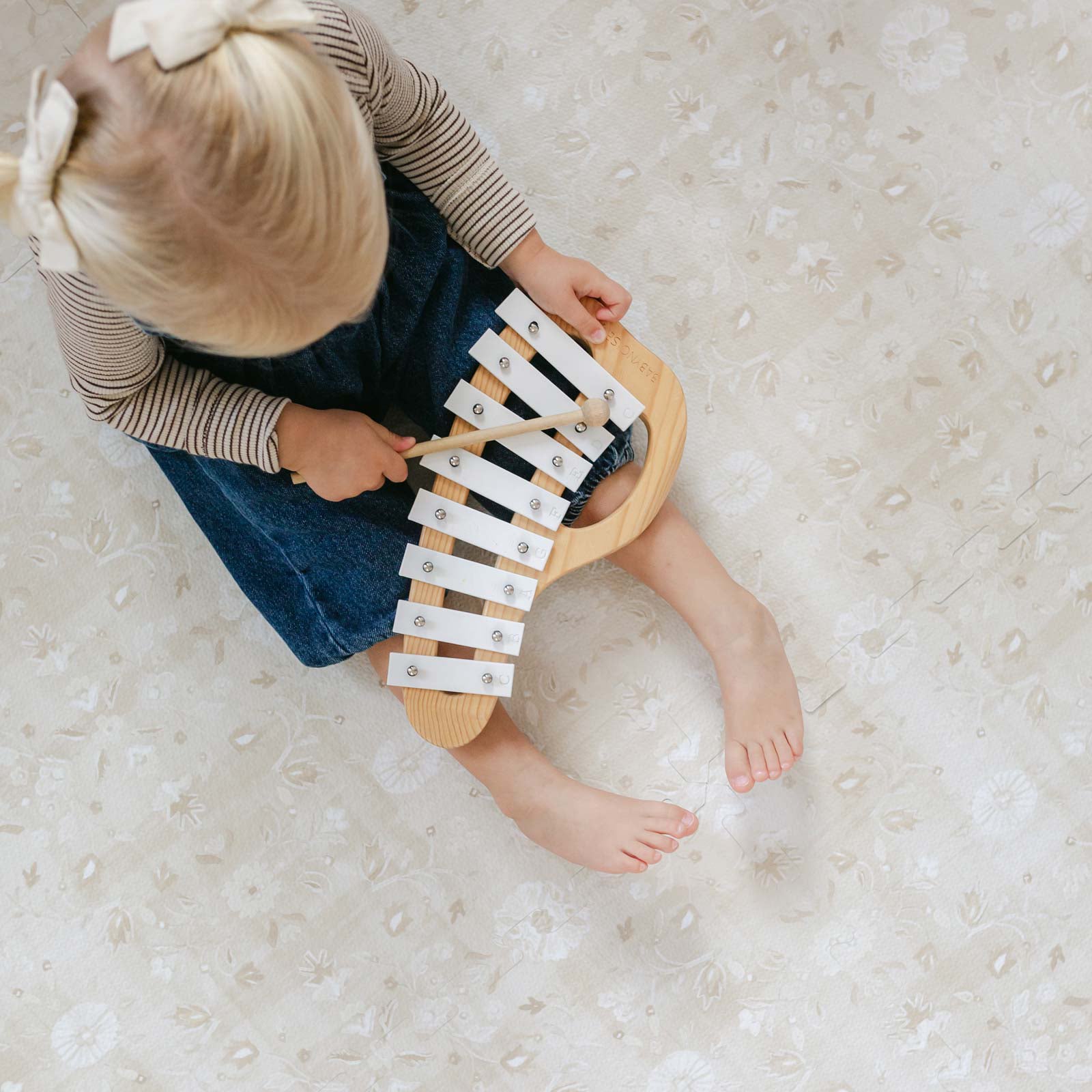 Gemma Chateau neutral floral play mat shown from above with toddler girl sitting on the mat playing with a xylophone