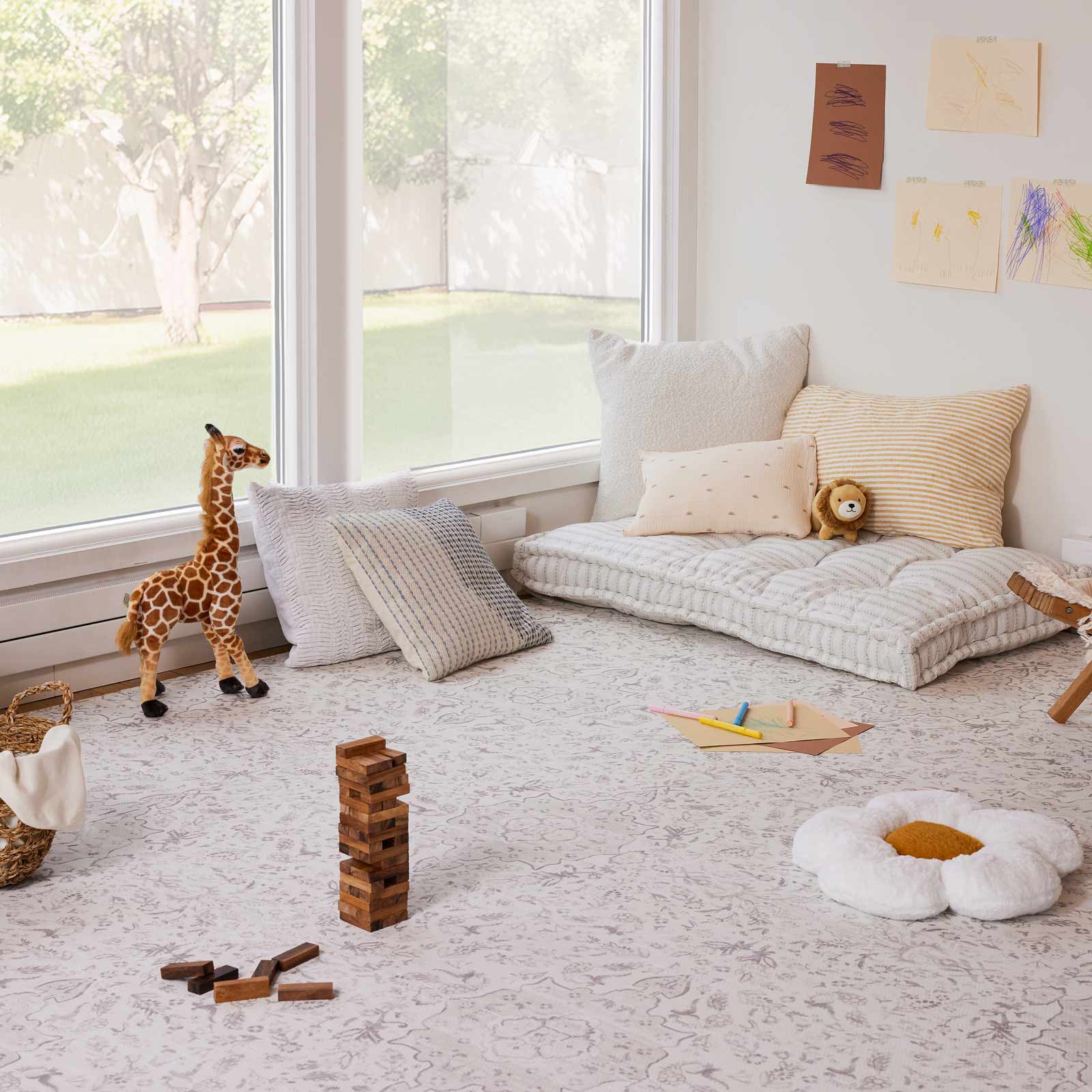 Emile Latte neutral floral little nomad play mat shown in a play room with pillows and toys laid out on the mat