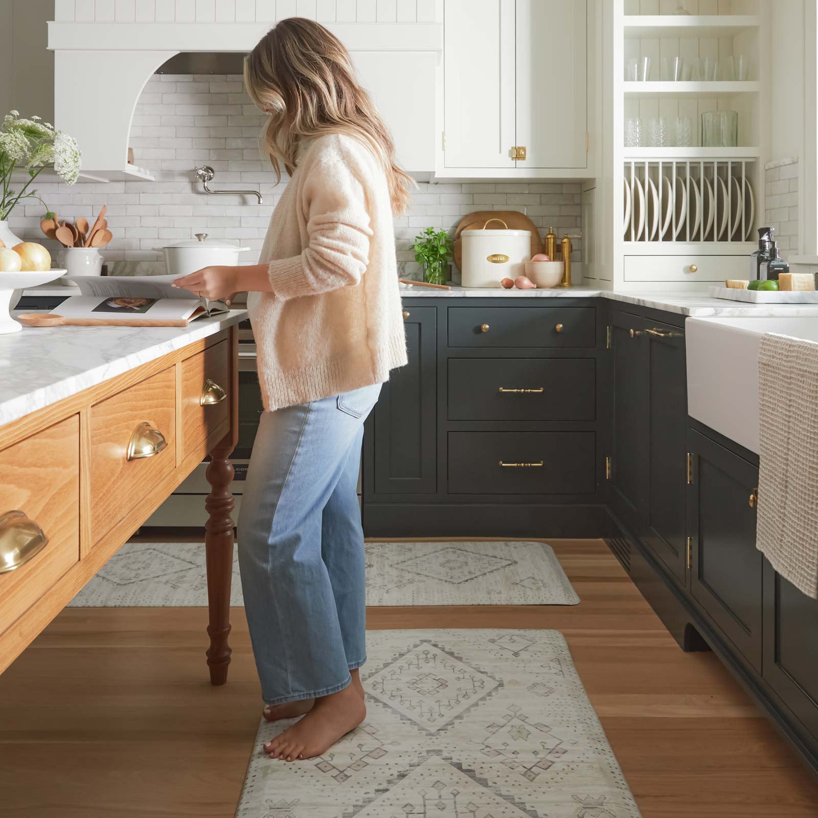 Ula Calico neutral boho print standing mat shown in a kitchen in sizes 30x72 and 22x72 in front of the counters and island with woman standing at the island reading a cook book