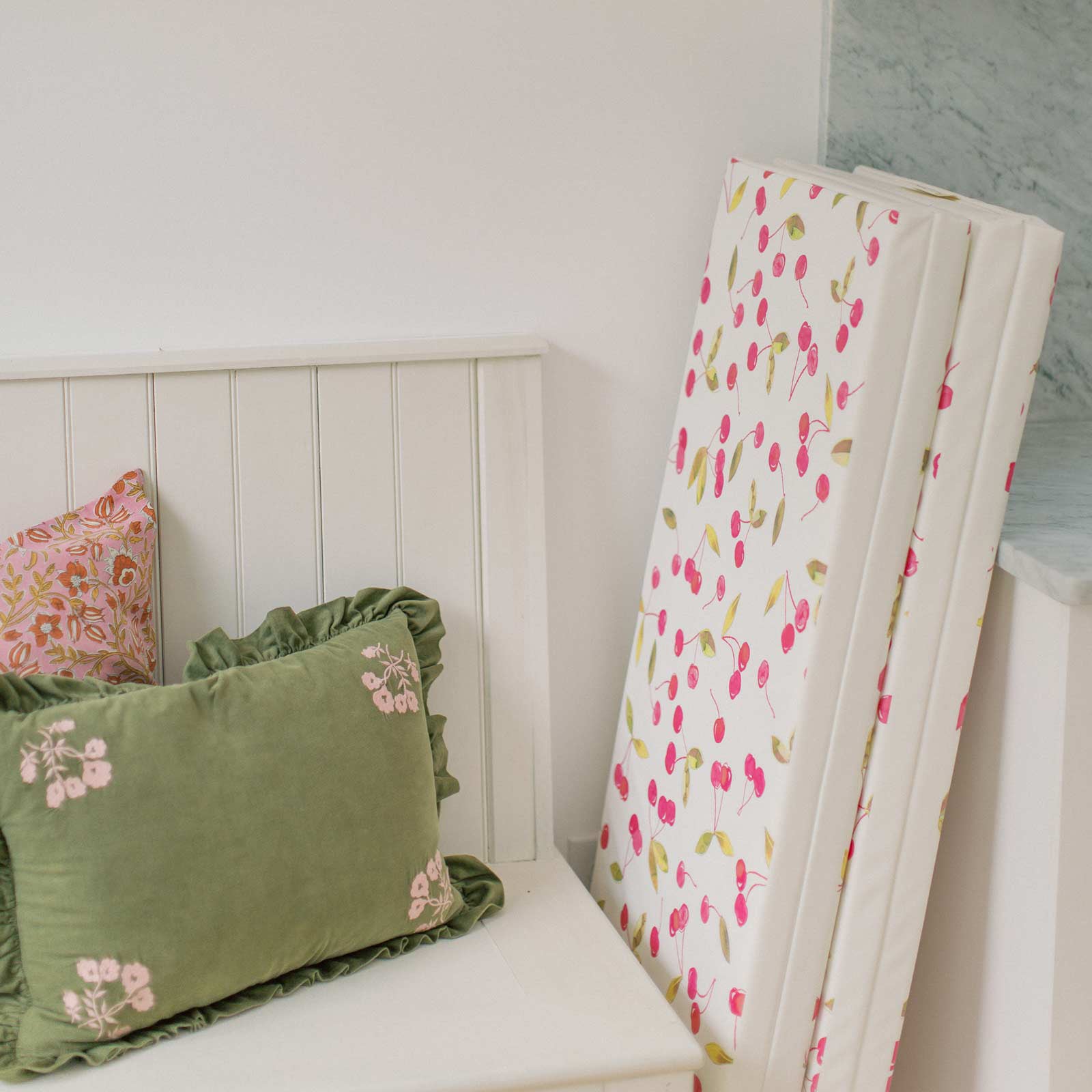 Lulu red and green Cherry print tumbling mat shown folded up and tucked into a corner next to a bed to be stored away