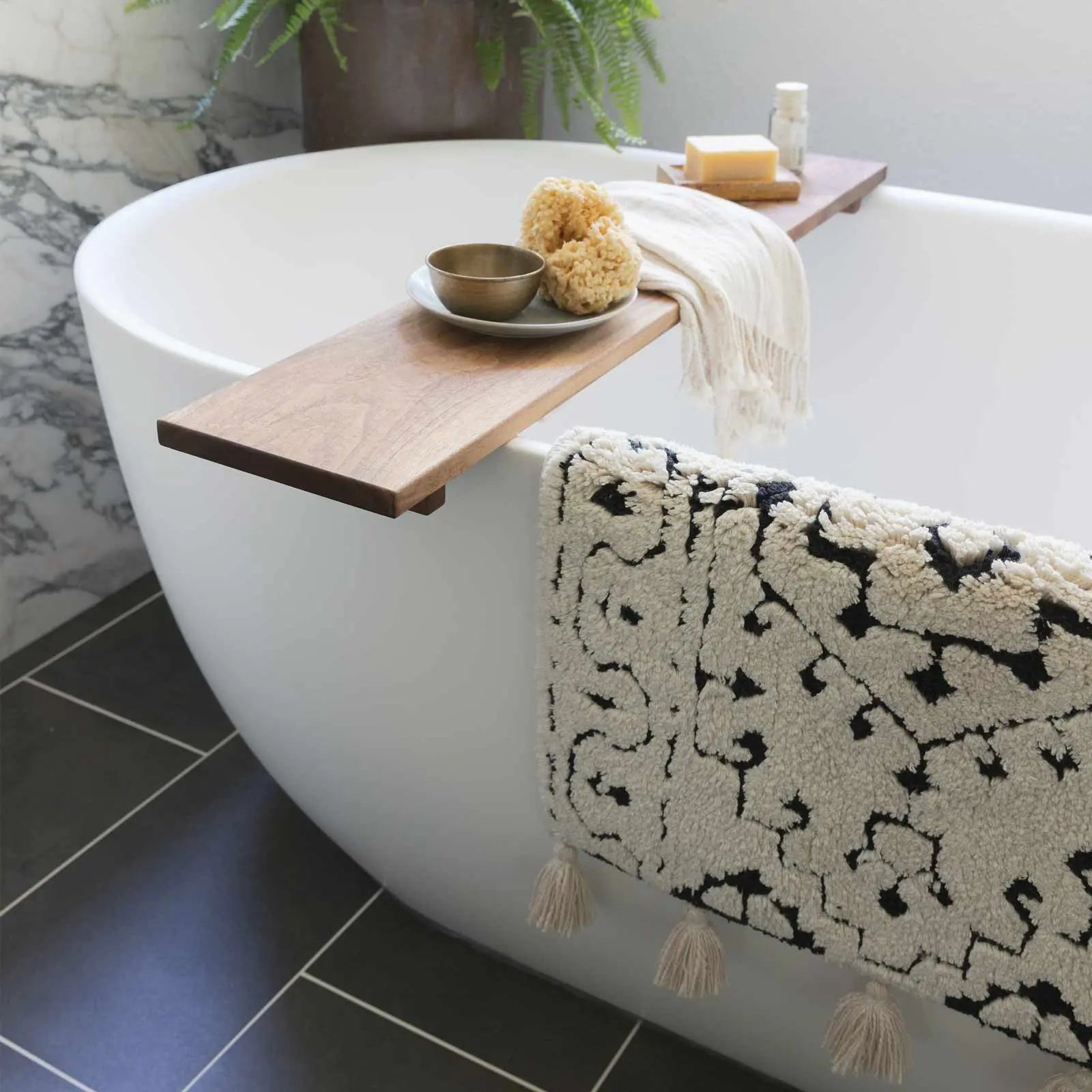 Arden noir black and white persian rug pattern bath mat in size 21x34 hanging over the side of a tub with wooden spa shelf laying across the tub