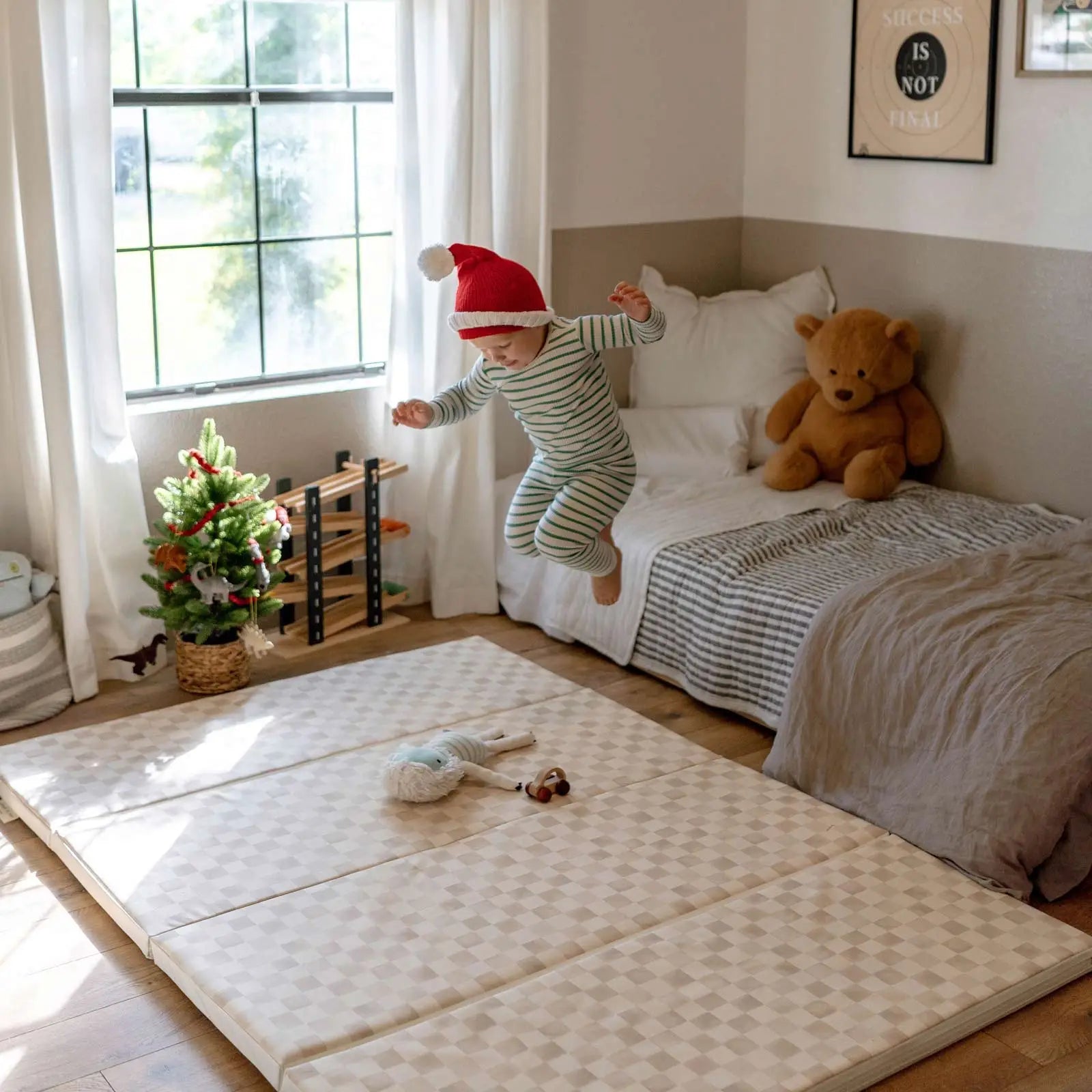 Almond neutral checker print tumbling mat shown in size 4x6 with little boy wearing a santa hat jumping off his bed onto the mat 