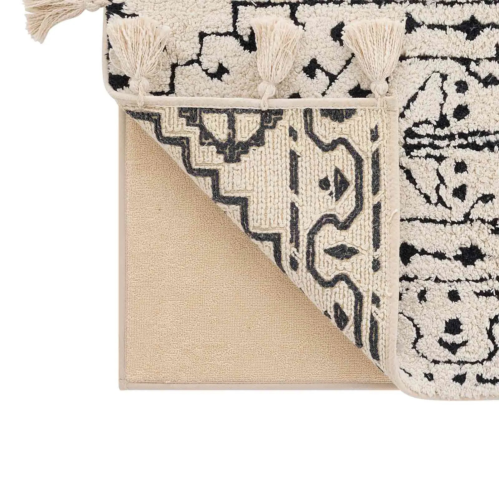 Corner of the arden noir black and white persian rug pattern bath mat lifted up to show the foam liner beneath
